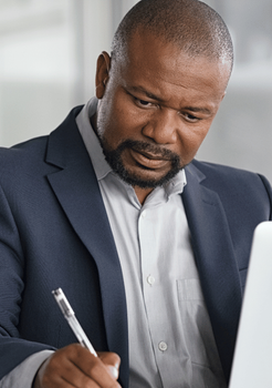 Man in navy blazer writing on paper at a desk, focused on work