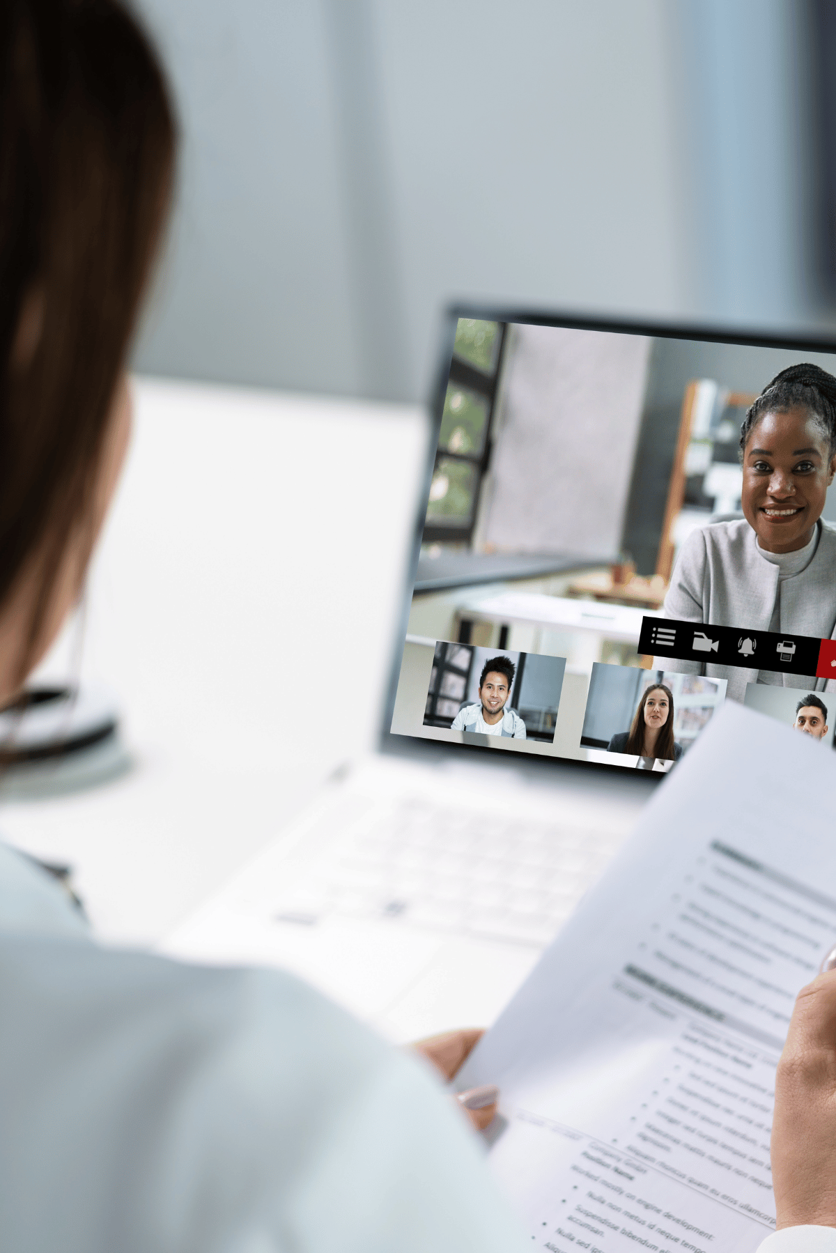 Person in a video meeting reviewing printed documents on a laptop screen