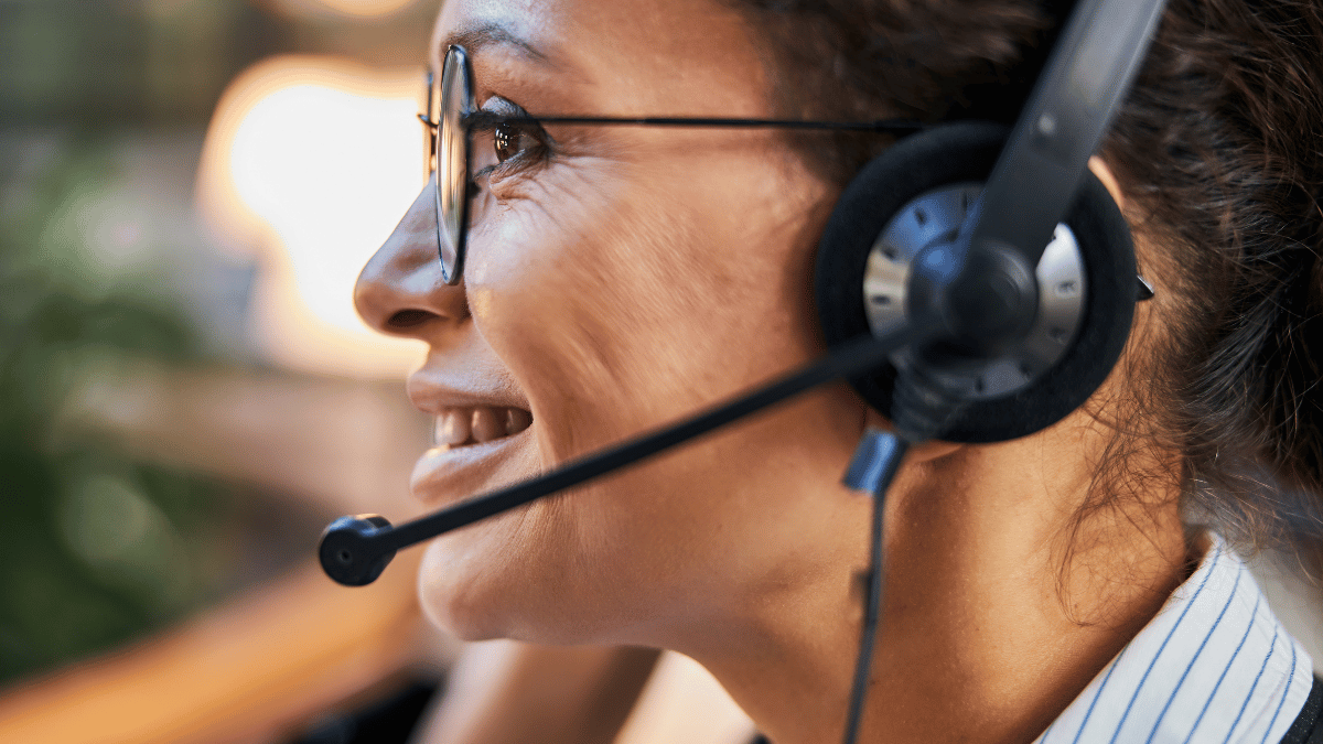 Woman wearing a headset microphone, smiling in profile in a bright office setting