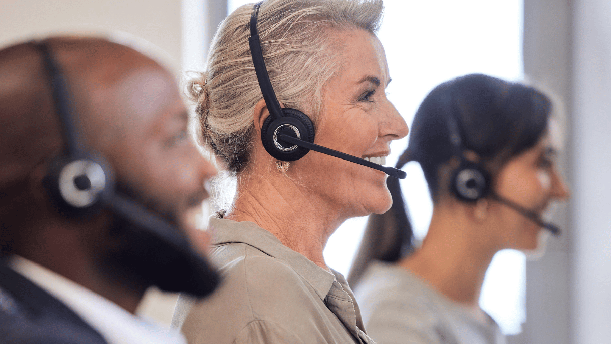 People wearing headsets in an office, seated in a row and facing forward.