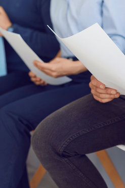 Two people seated holding white papers, likely reviewing documents in a meeting