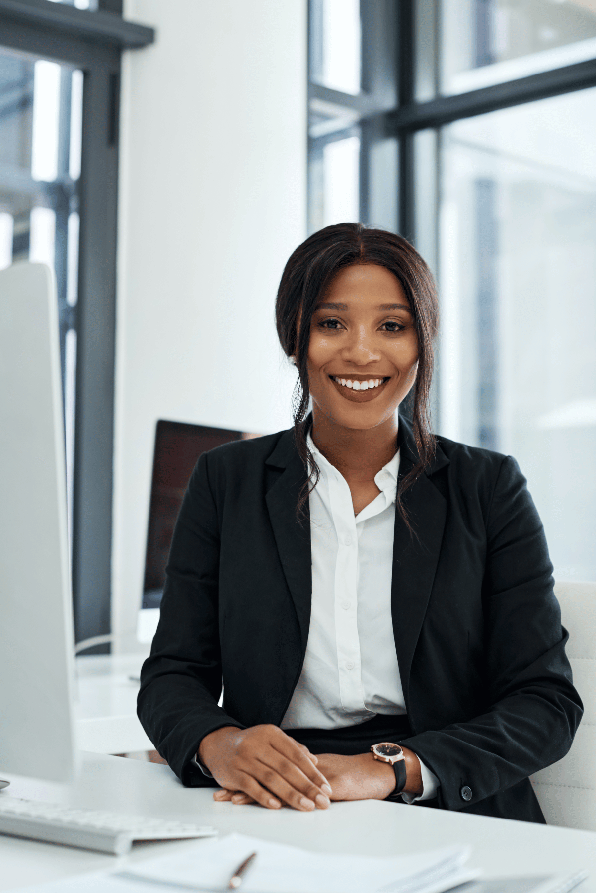 Smiling professional in a black blazer seated at a desk in a bright modern office