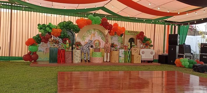 Escenario decorado con arco floral, cajas de regalo y cortinas verdes y rojas bajo una carpa.