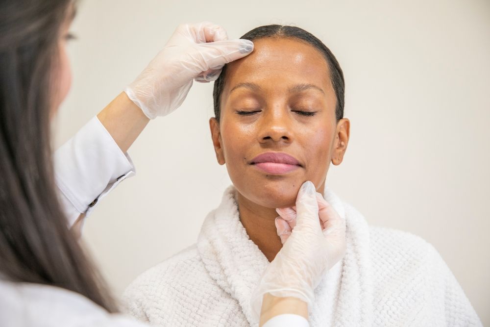 Woman having her face examined by someone wearing gloves in a clinic.