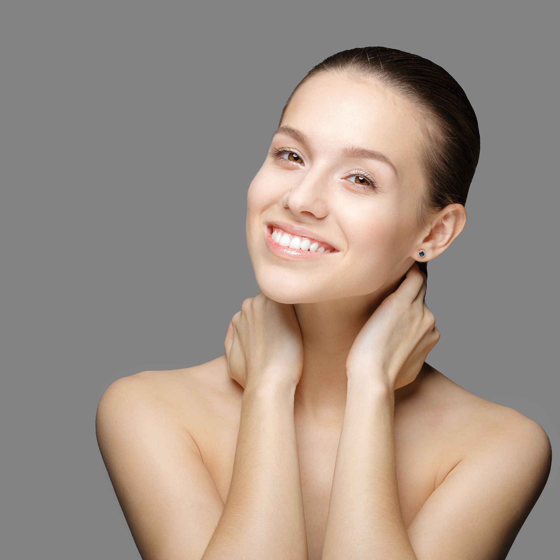 A woman without a shirt is smiling with her hands on her neck.