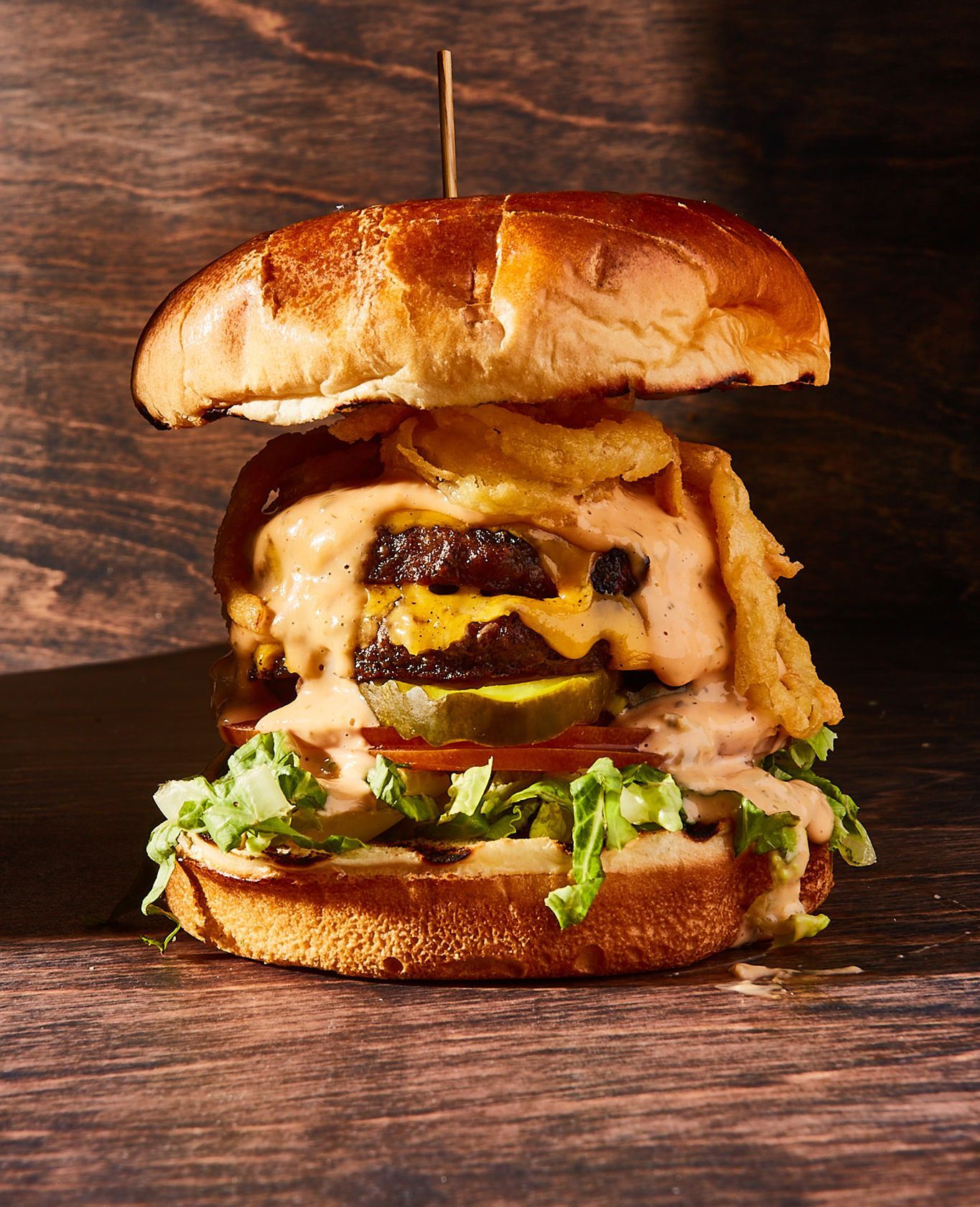 A hamburger with a toothpick in it is sitting on a wooden table.