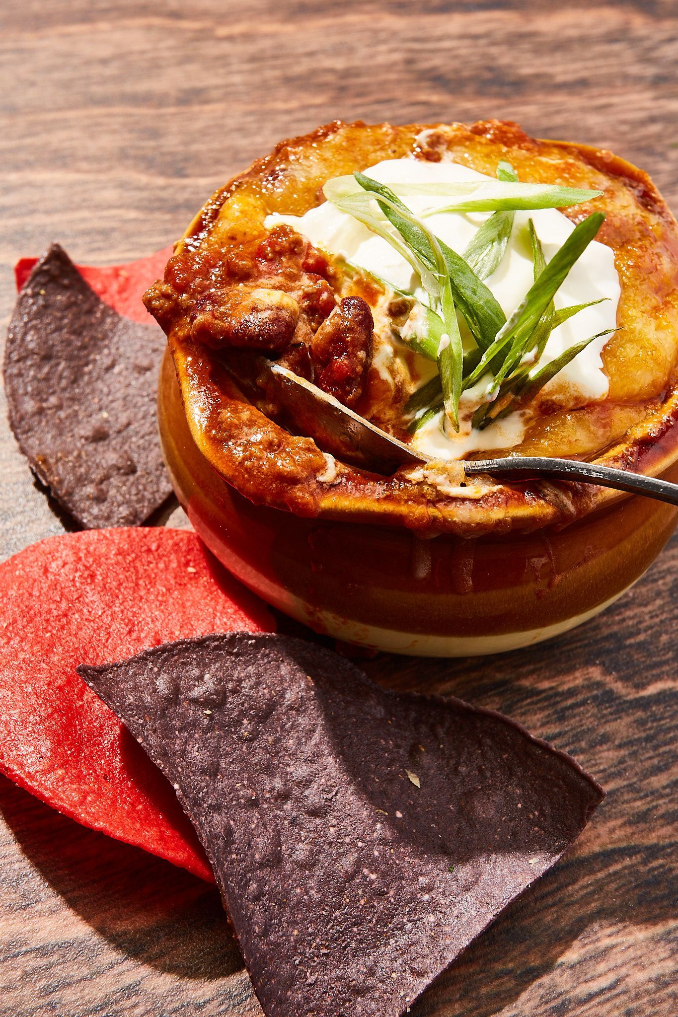 A bowl of chili with a spoon in it and tortilla chips on a table.