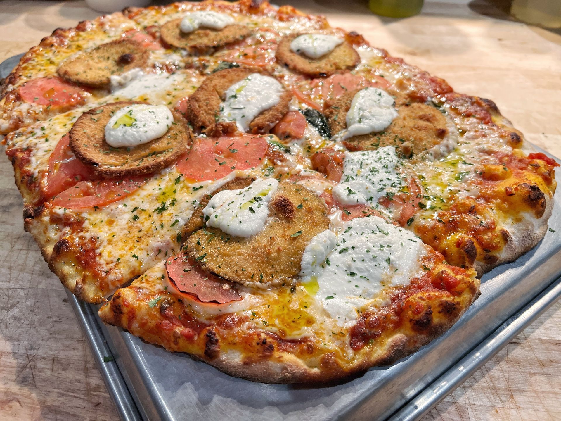 A pizza is sitting on a metal pan on a wooden table.