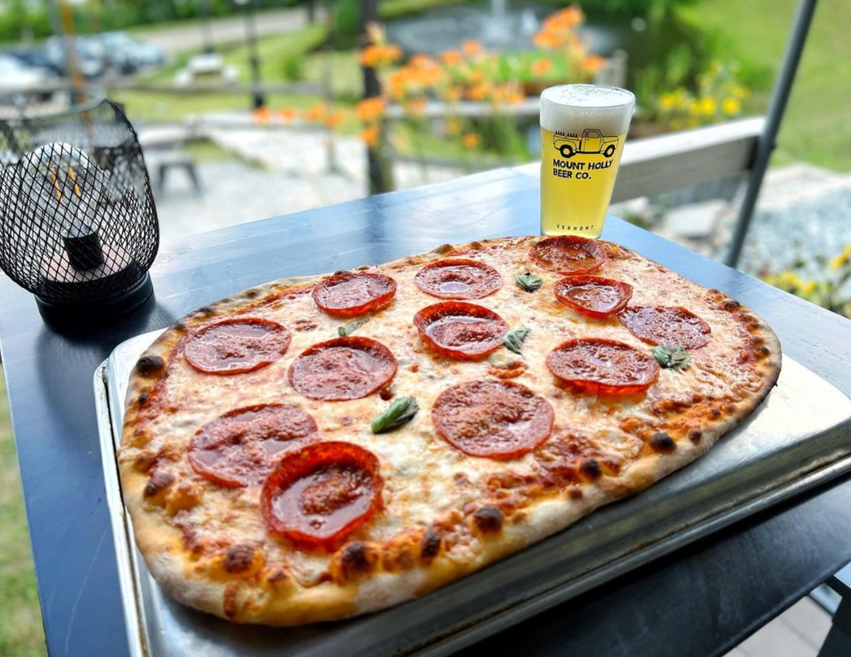 A pizza with pepperoni and tomatoes is sitting on a table next to a glass of beer.