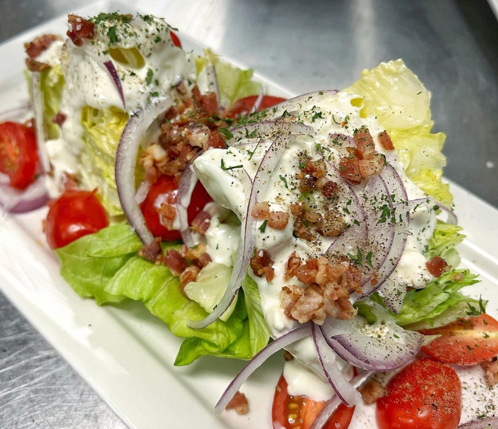 A salad with lettuce , tomatoes , onions and bacon on a white plate.