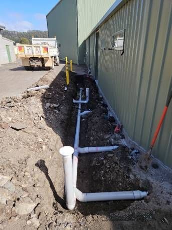 A bunch of pipes are being installed in the dirt in front of a building.