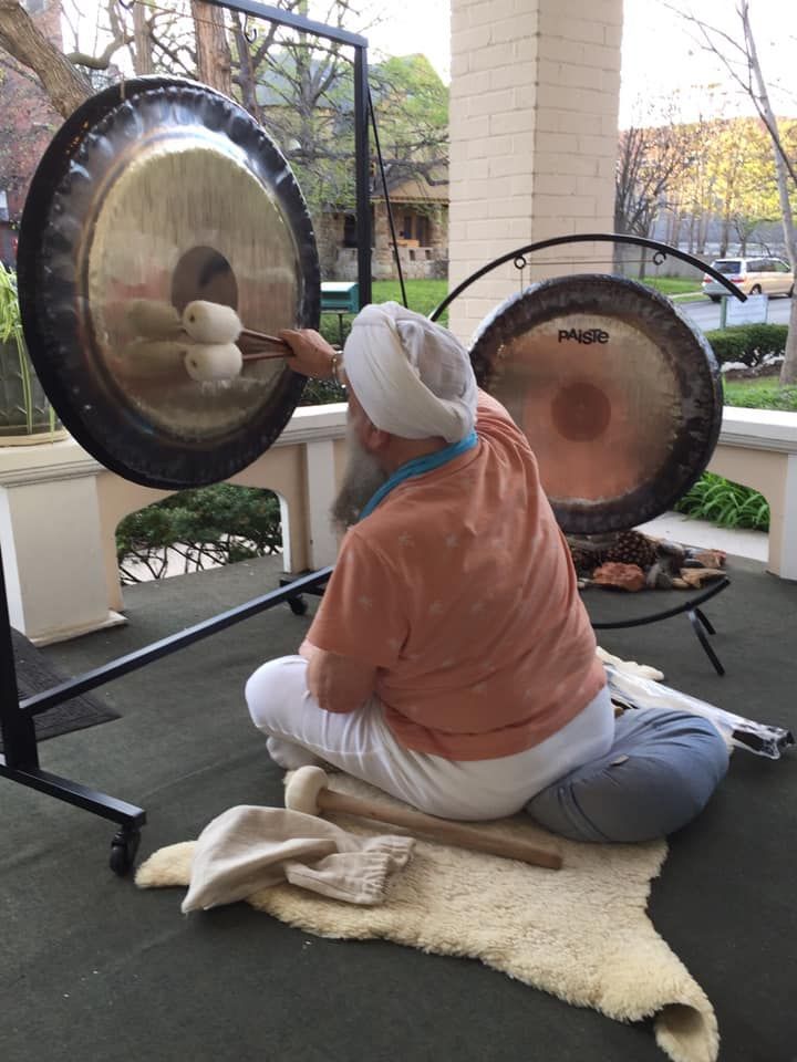 A man is kneeling down playing gongs on a porch.