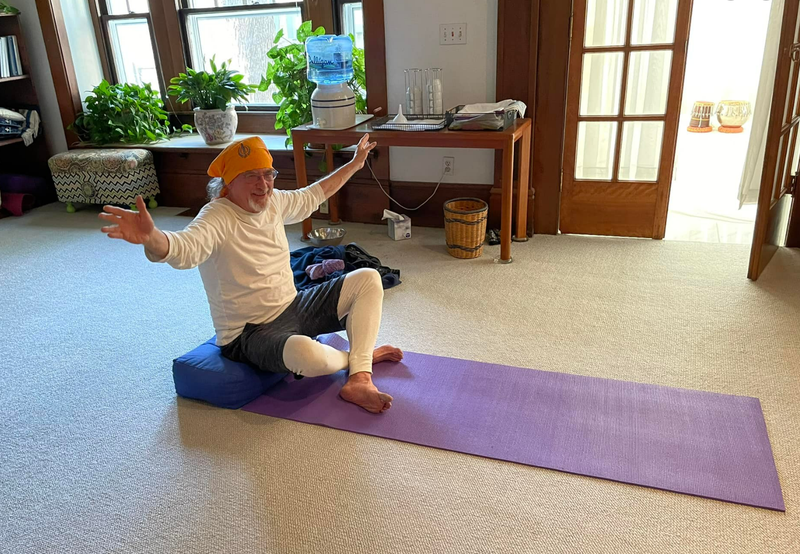 A man is sitting on a yoga mat in a living room.