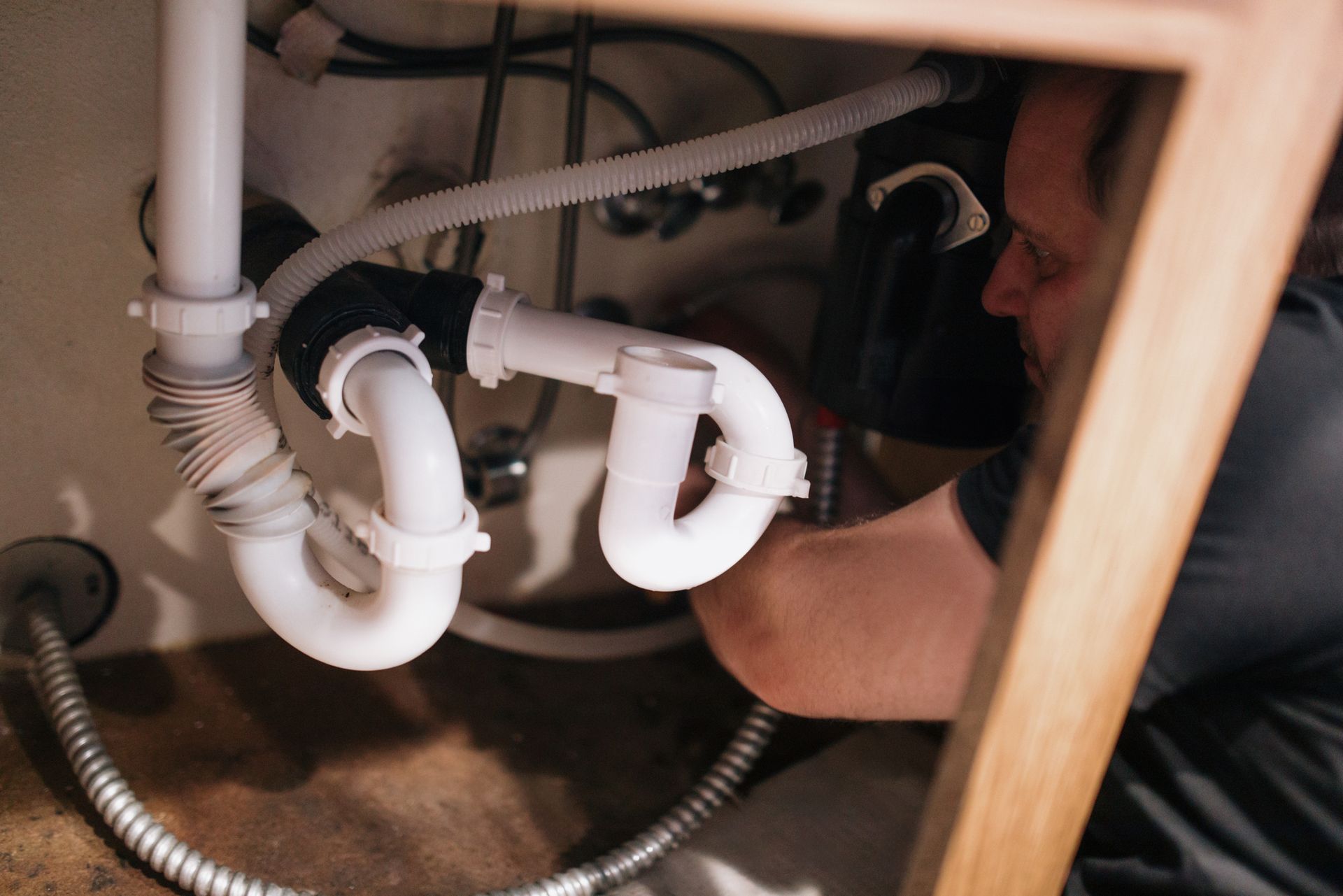 A man is fixing a sink pipe under a sink.