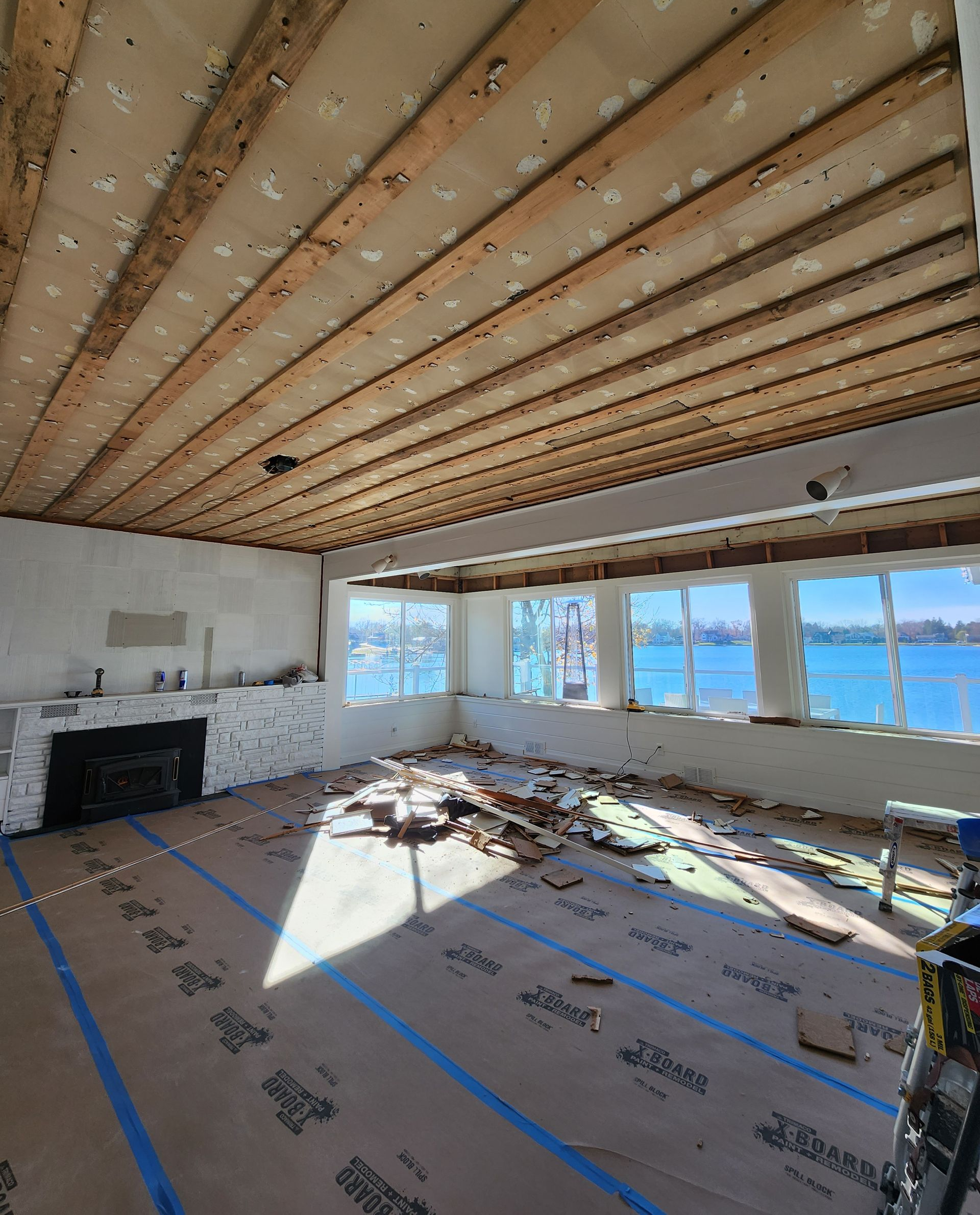 Unfinished living room with exposed ceiling beams, fireplace, large windows, and construction debris on the floor