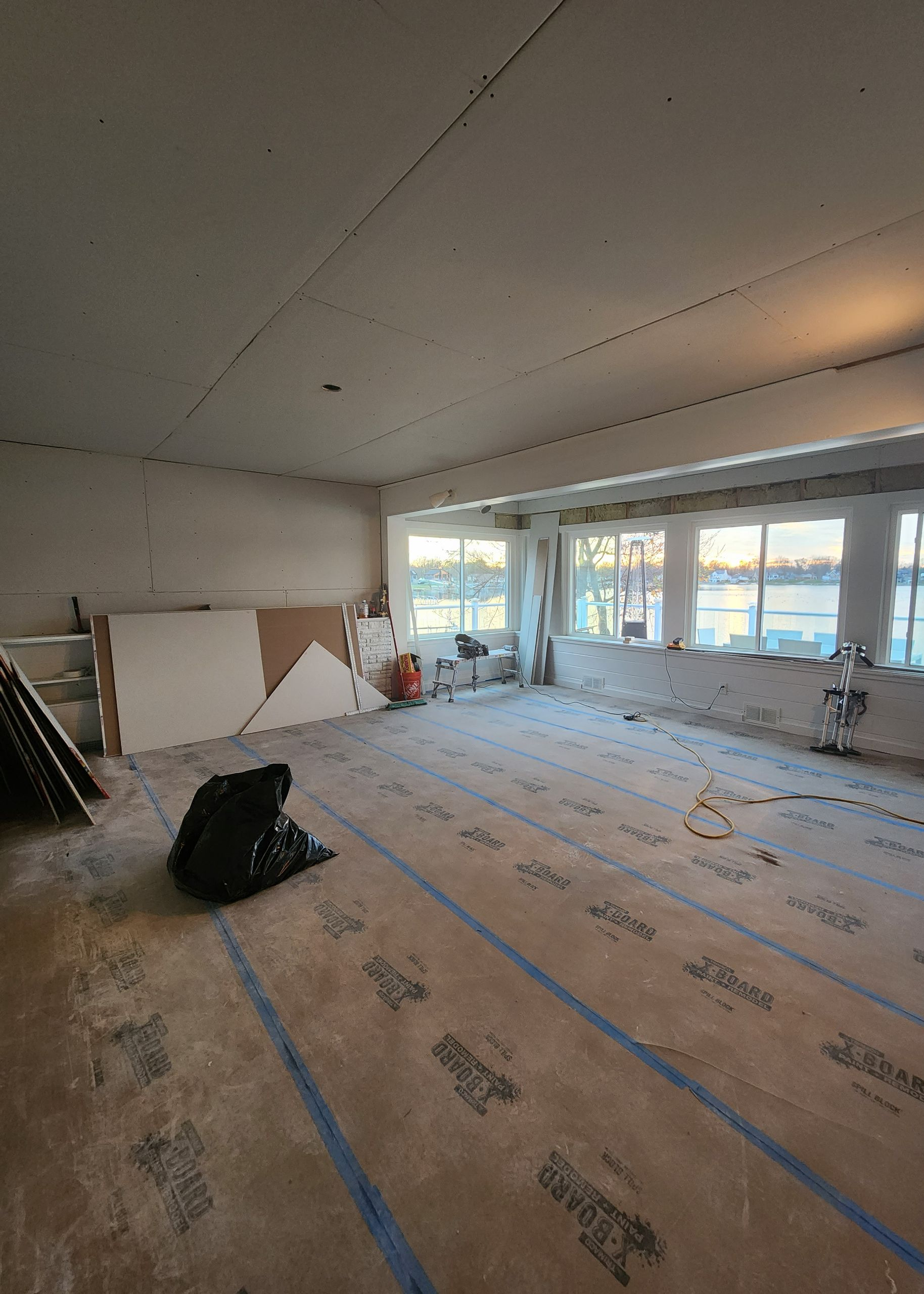 Empty room under renovation with covered floor, tools, and large windows letting in daylight