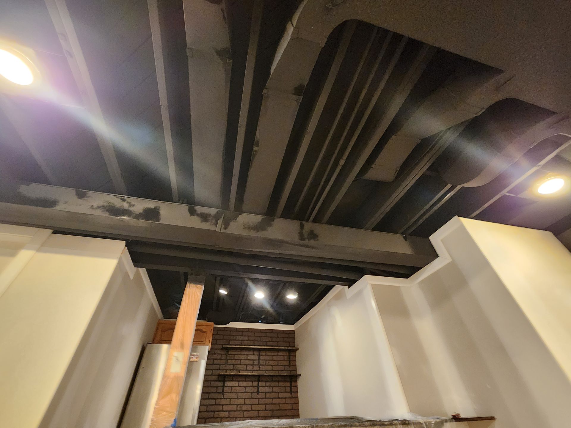 Ceiling with exposed pipes and recessed lights above a narrow interior stairwell