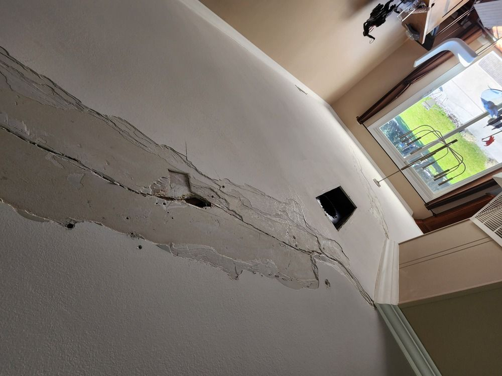Ceiling with a large crack and peeling plaster above a window in a room