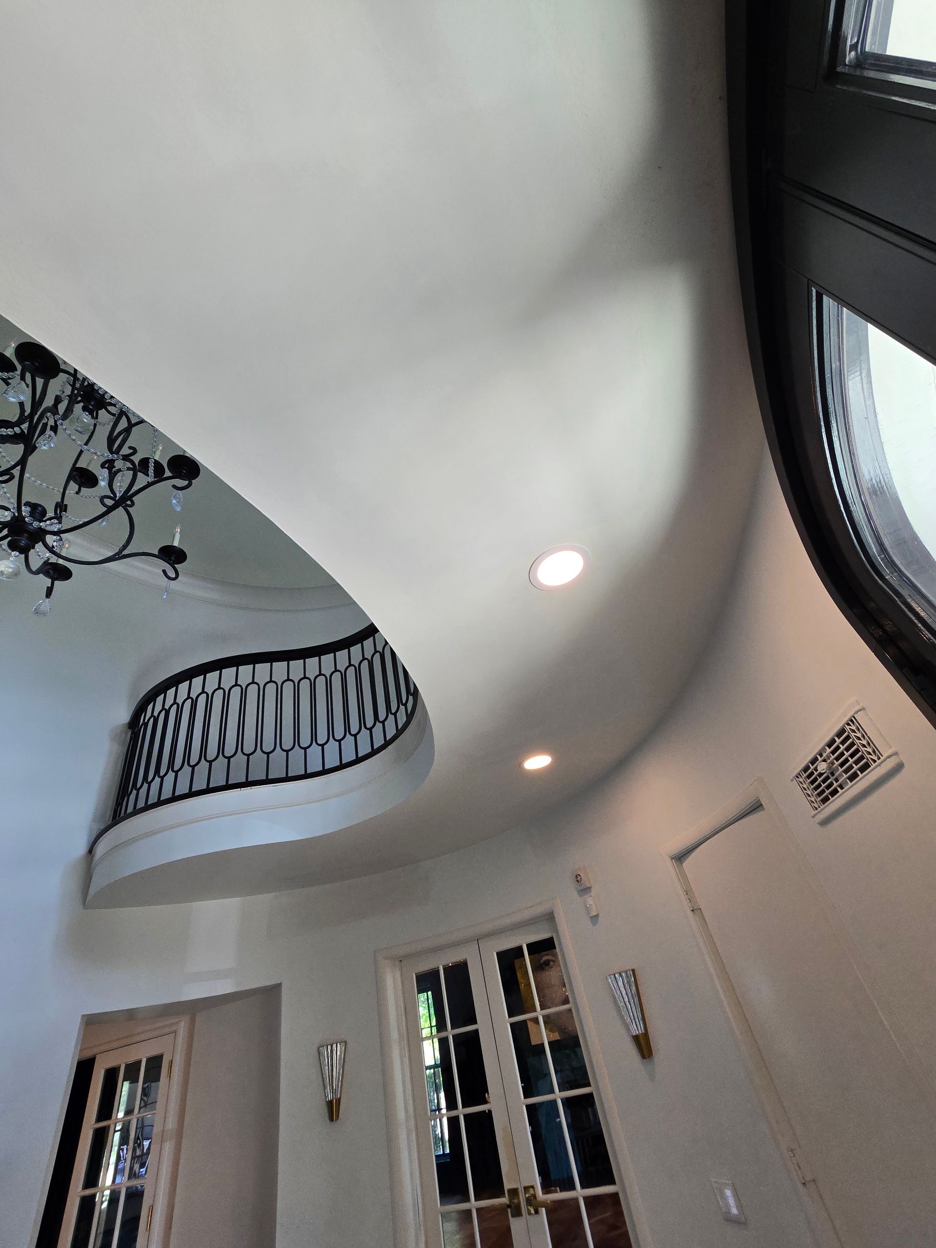 Curved indoor ceiling with recessed lights, balcony railing, and tall windows in a bright hallway