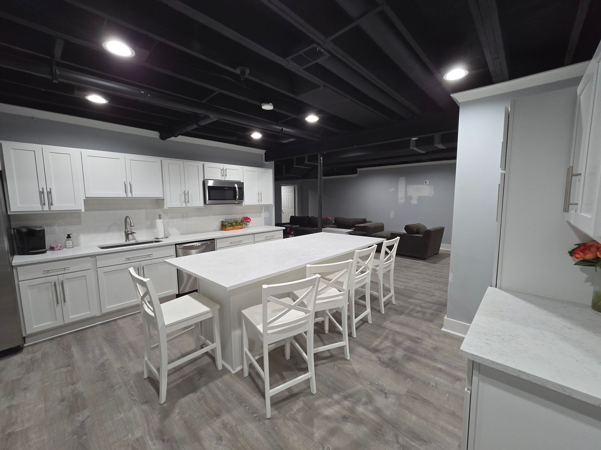 Modern kitchen with white cabinets, large island, and four white bar stools under dark ceiling beams