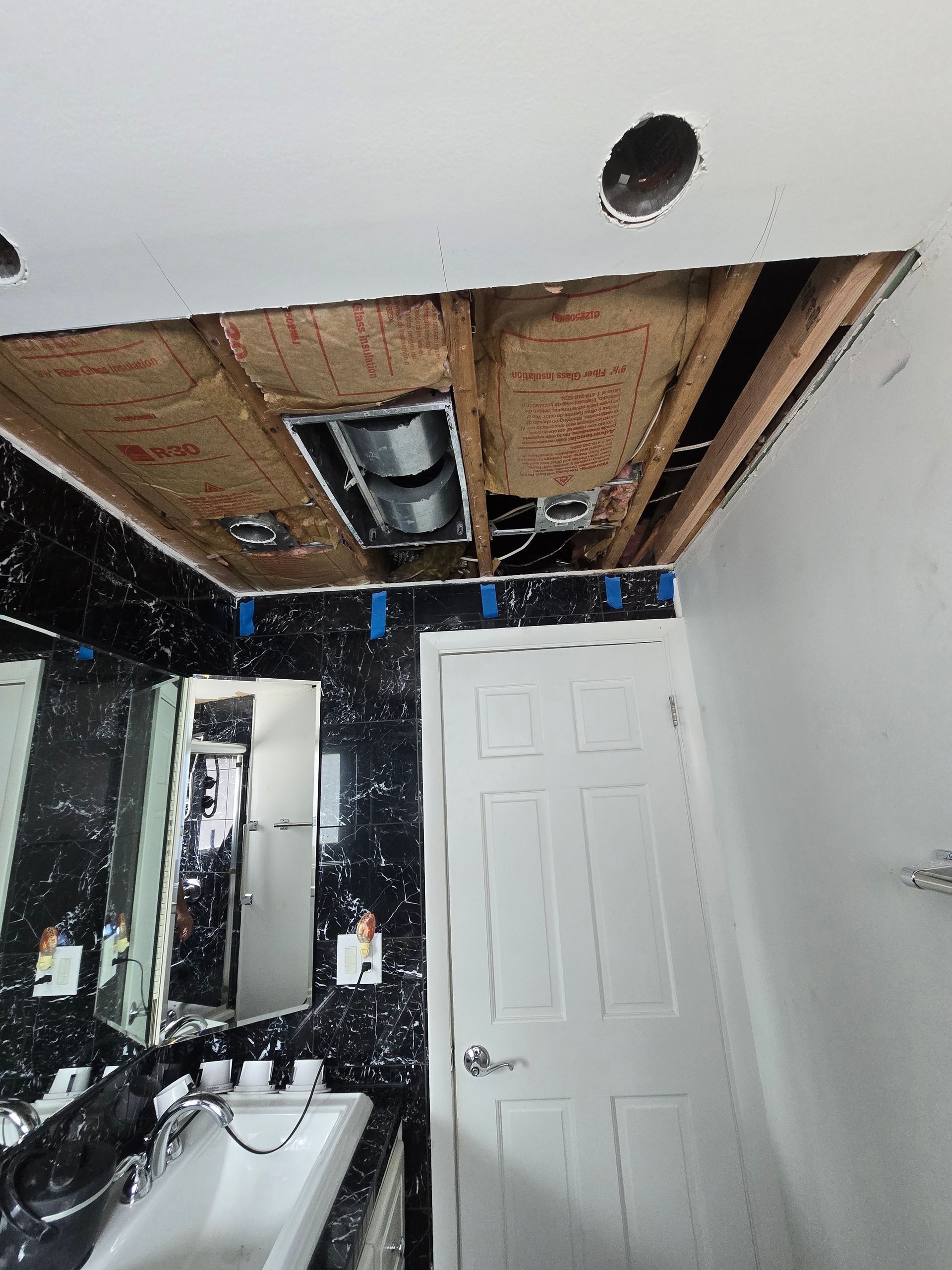 Bathroom with exposed ceiling beams, mirror, sink, and white door, showing ongoing renovation or damage repair