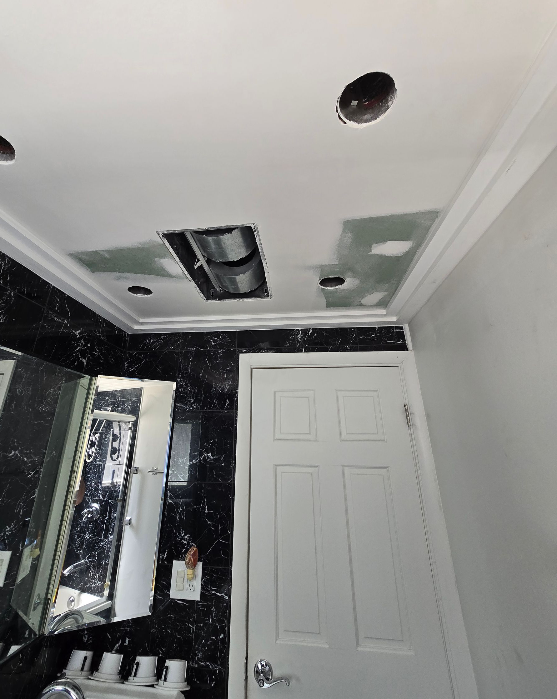 Partially renovated room with white ceiling, exposed vents, and a closed white door.