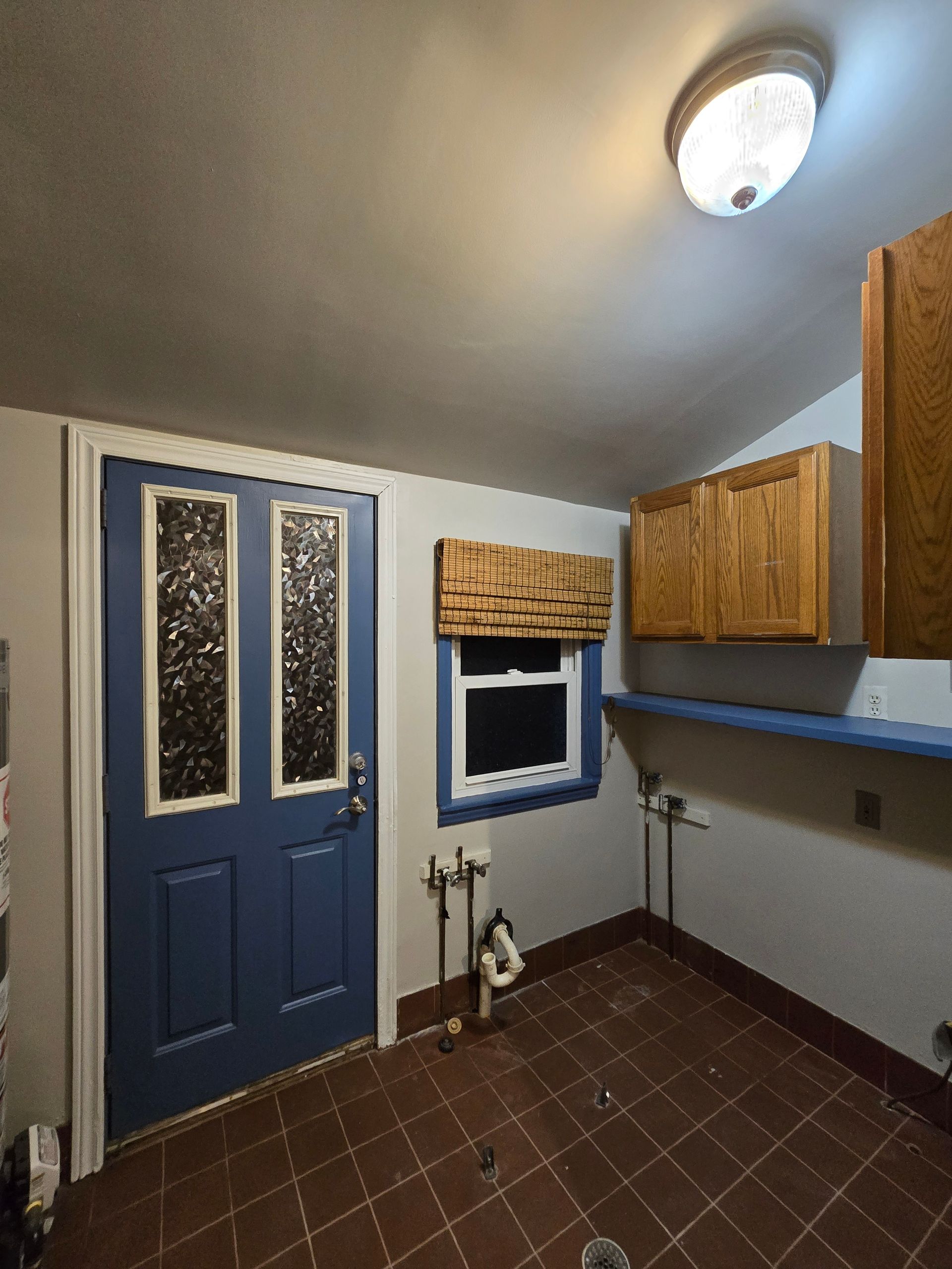 Small laundry room with blue door, window, wood cabinets, utility sink, and tiled floor.