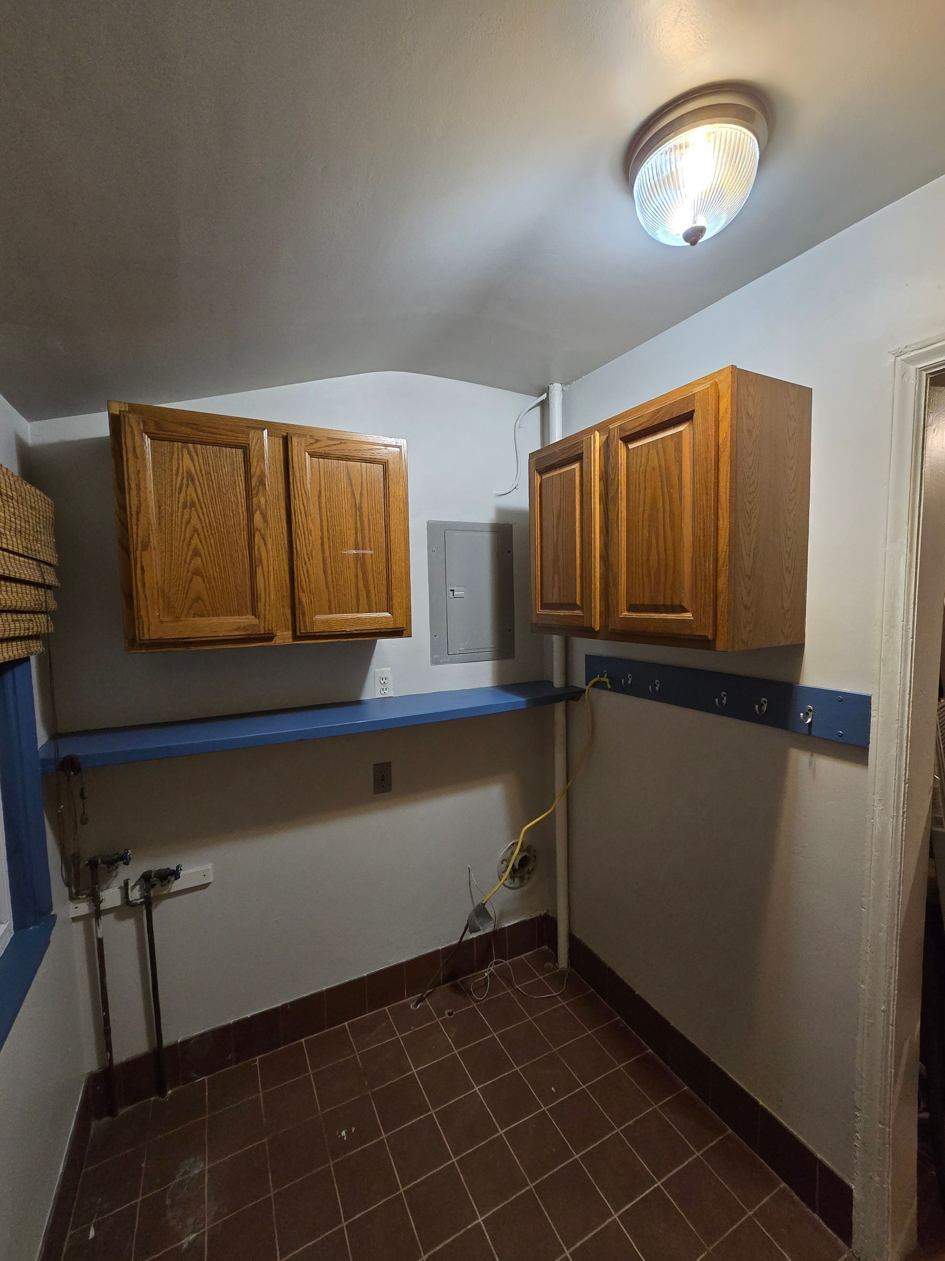 Small empty laundry room with wall cabinets, blue counter, tiled floor, and ceiling light.