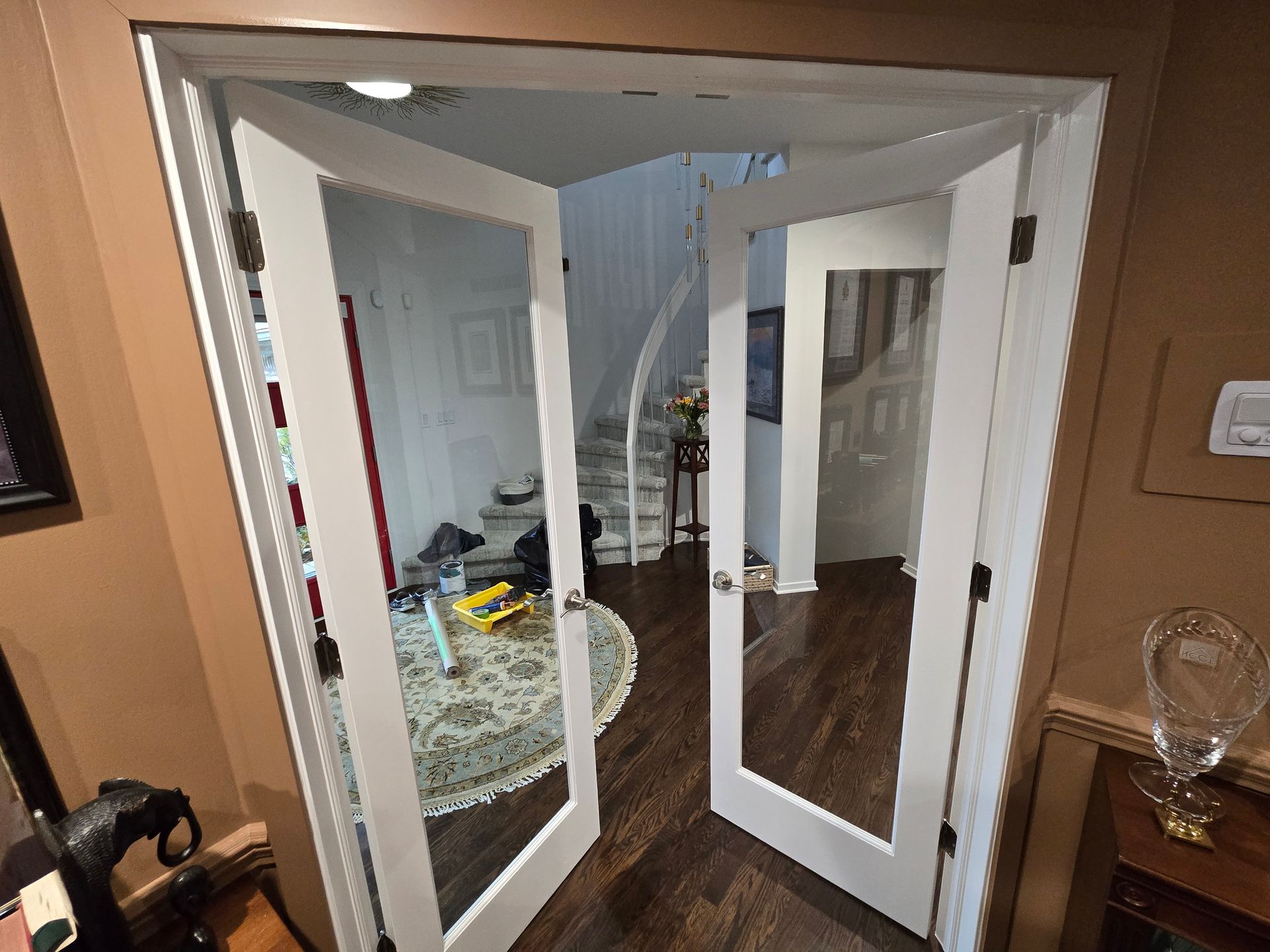 Open white French doors into a hallway with a round mirror and dark wood floor.