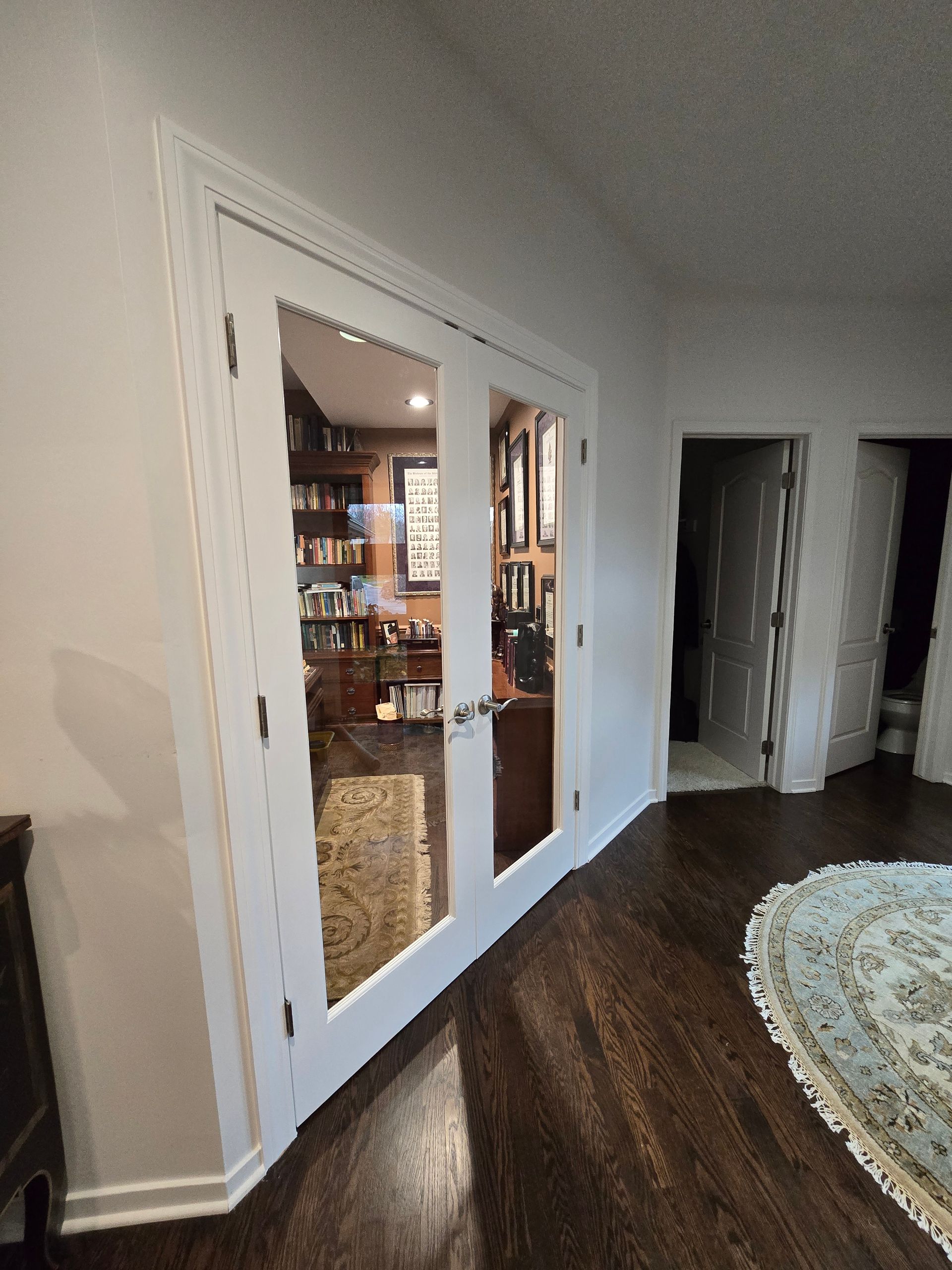 Hallway with white French doors opening to a kitchen and a dark wood floor beside a round rug