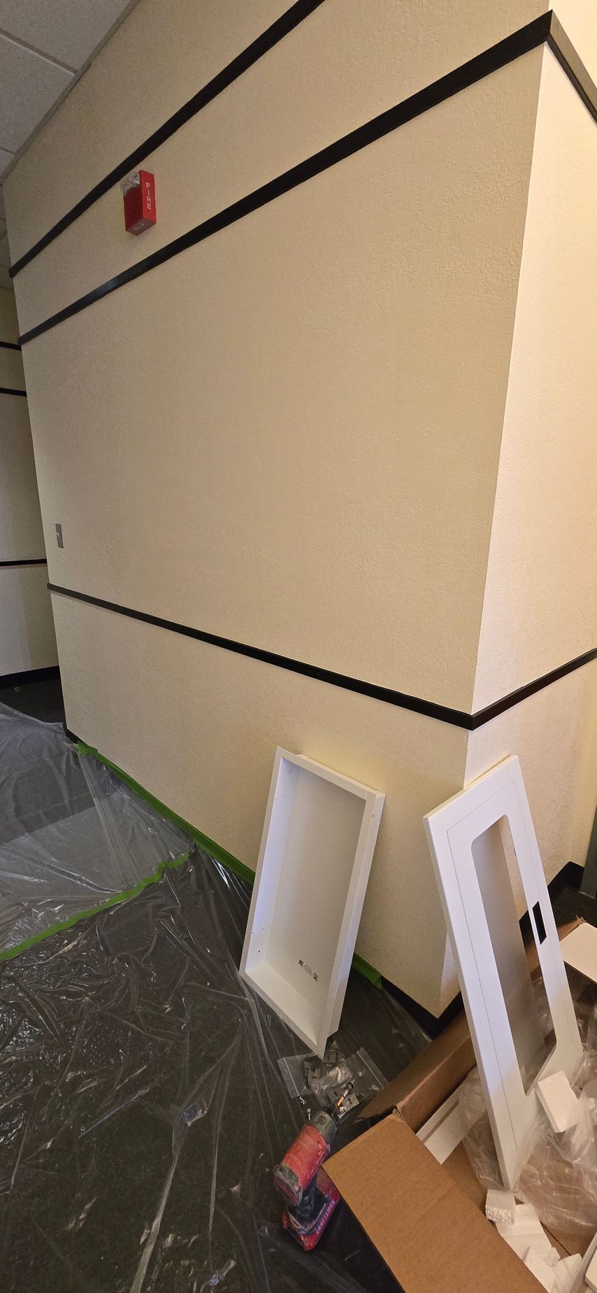 Beige exterior wall with black trim and leaning white signs beside a sidewalk in a hallway-like area