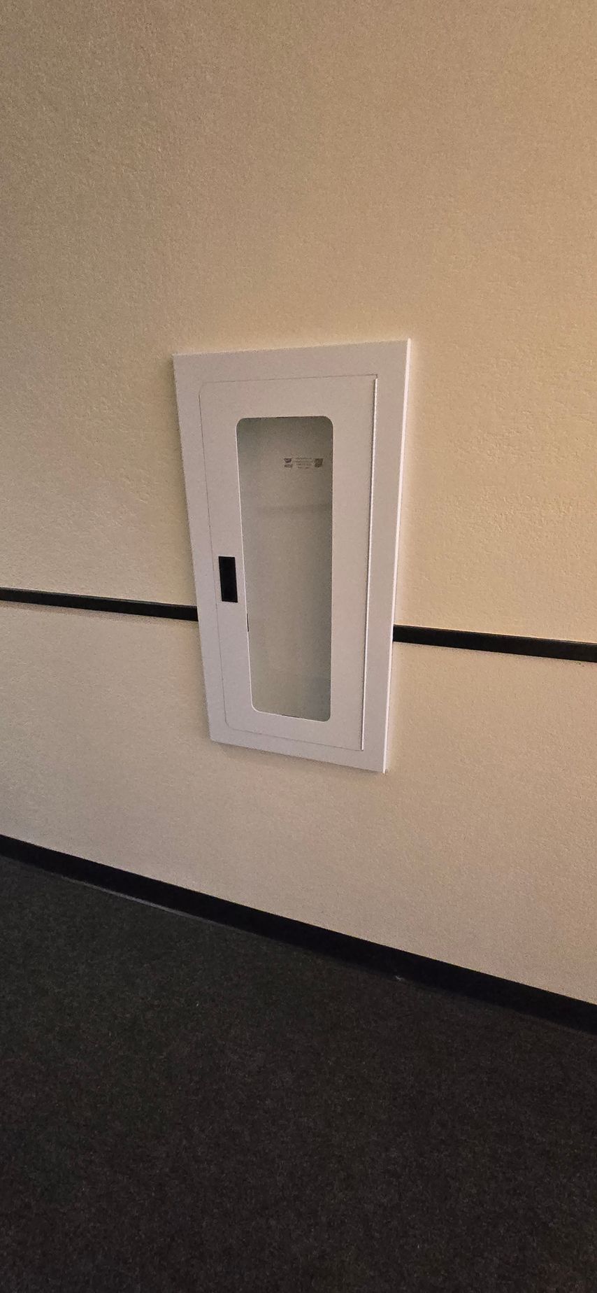 White wall-mounted electrical panel or utility box on a beige wall above a dark floor.