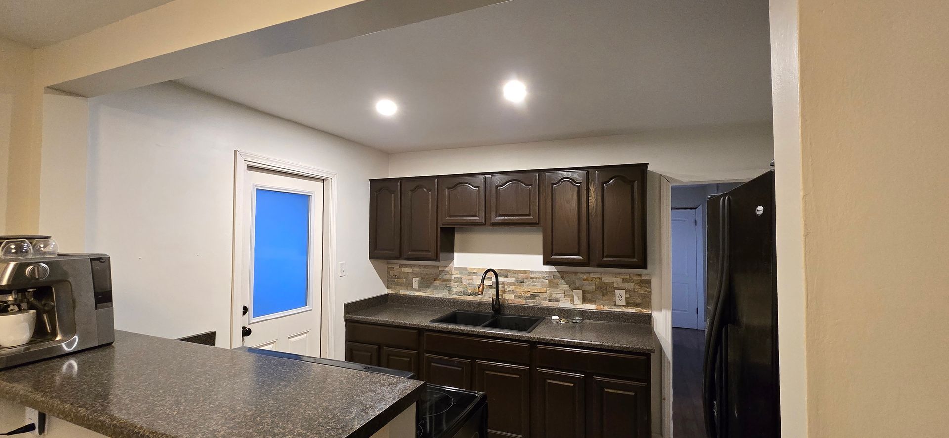 Kitchen with dark wood cabinets, granite counters, and a doorway with blue daylight beyond.