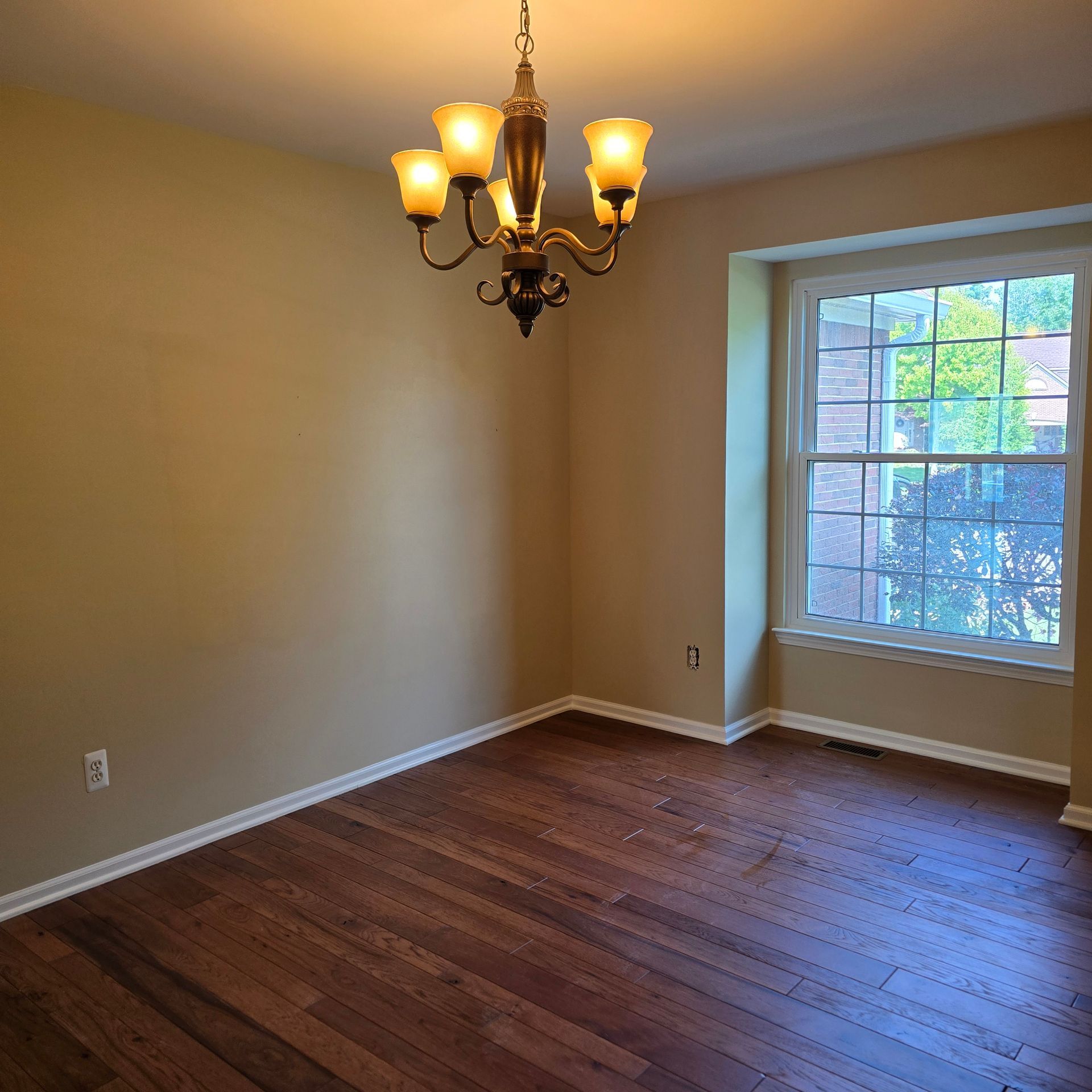Empty room with hardwood floors, beige walls, a chandelier, and a large window