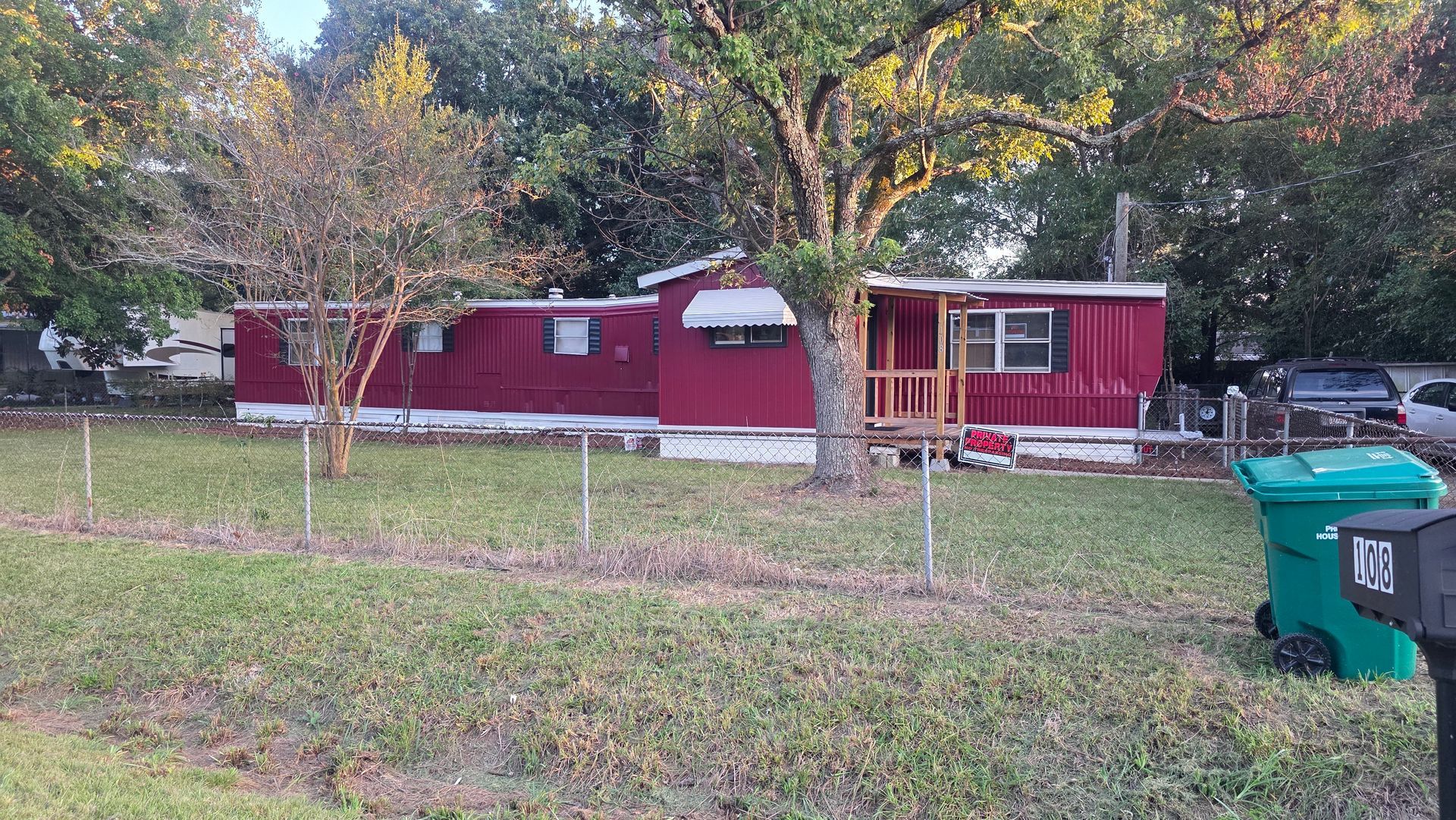 Red trailer home with a porch and fenced yard in the woods