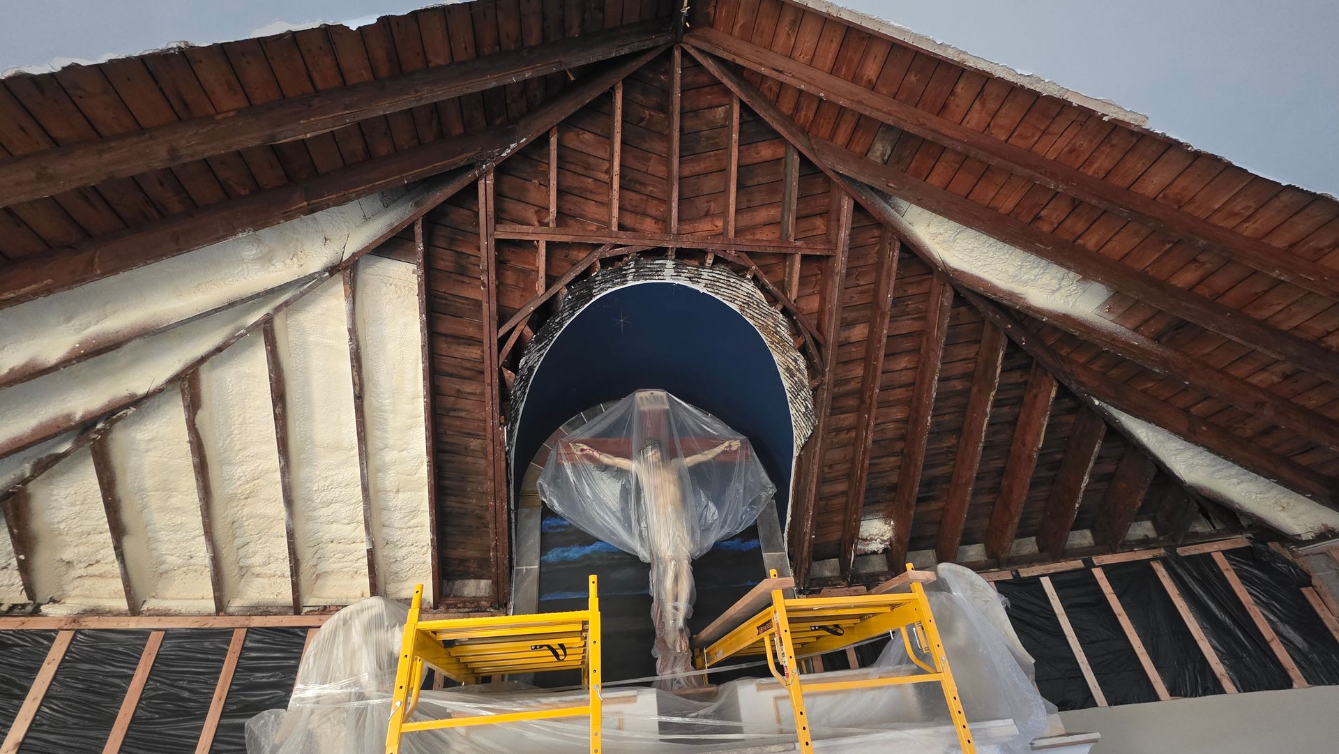 Attic roof interior with exposed wood beams, insulation, and a central arched opening with construction barriers