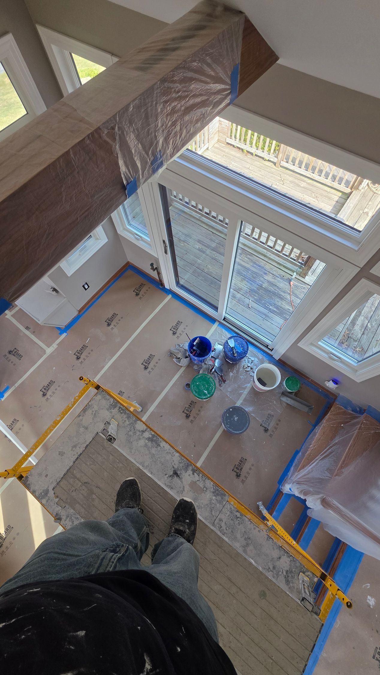 Looking down from a high stairwell onto a tiled lobby with windows, buckets, and a person’s shoes at the edge.