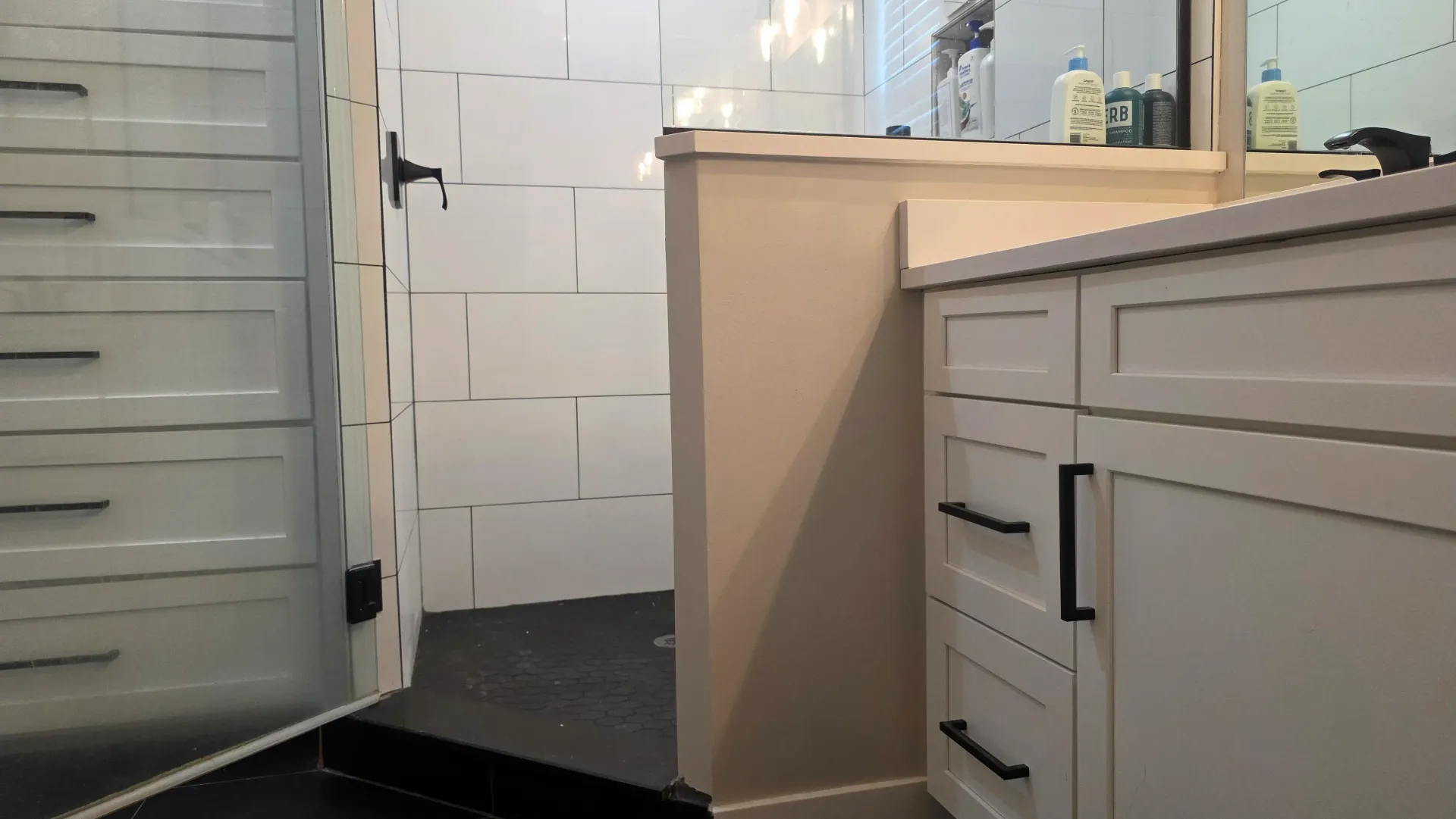 Narrow bathroom with white cabinets, tiled floor, and beige vanity edge near a doorway.