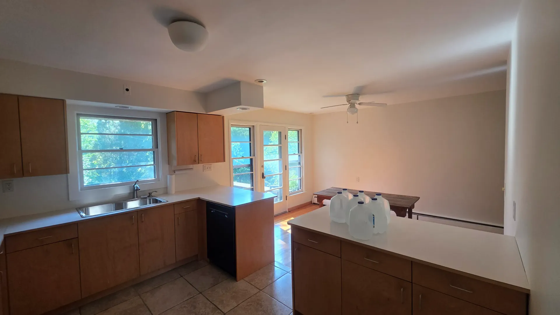 Empty kitchen with wooden cabinets, white countertops, tiled floor, and daylight through windows and glass doors