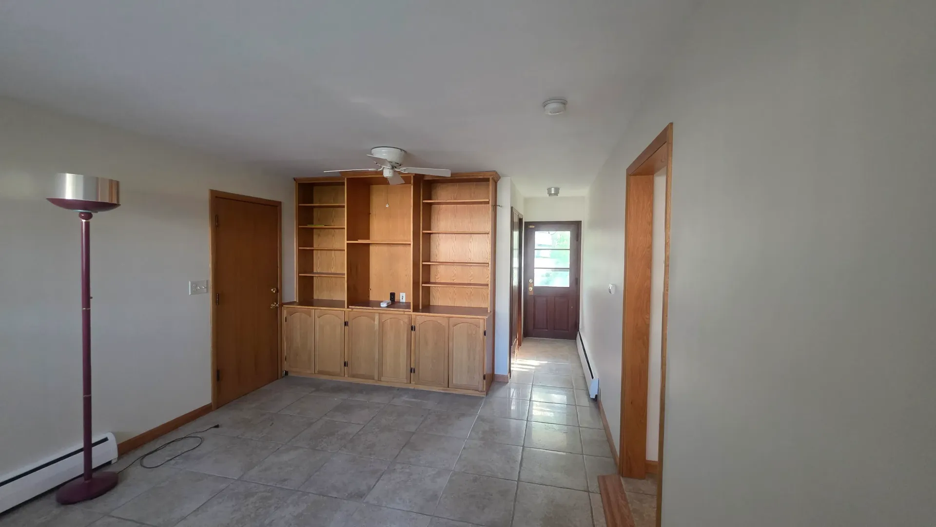 Empty living room with light wood cabinets, tiled floor, and a floor lamp by the wall