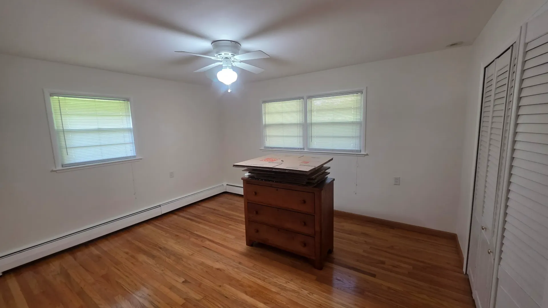 Empty bedroom with hardwood floor, two windows, ceiling fan, and a wooden dresser centered against the wall