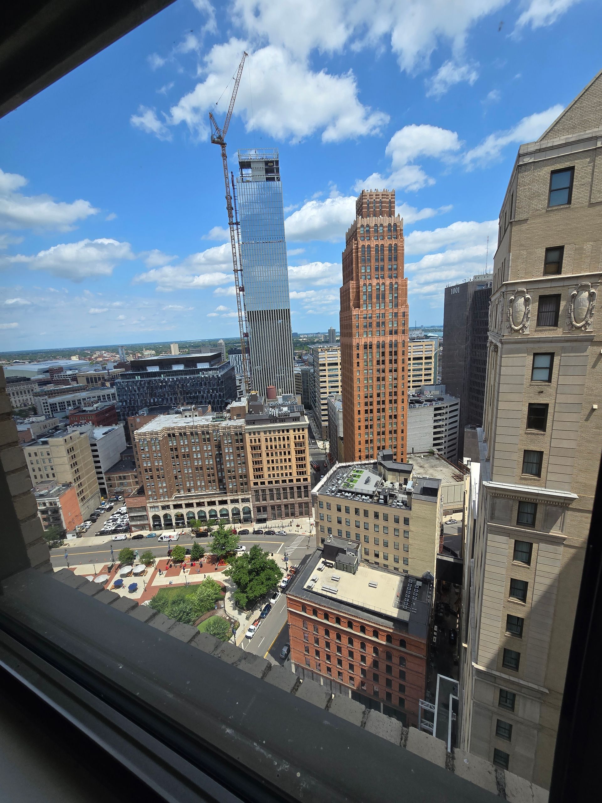 City skyline viewed from a high-rise window, with cranes and tall buildings under a blue sky.