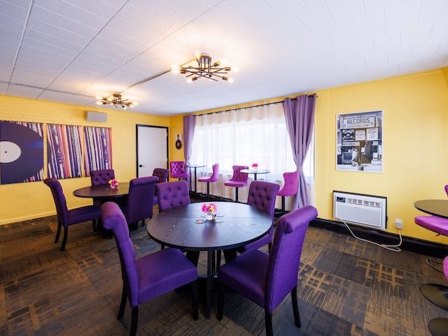 Purple chairs around a round table in a yellow room with purple curtains and ceiling lights.