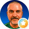 Smiling bald man with orange beard, blue background, and small star badge icon