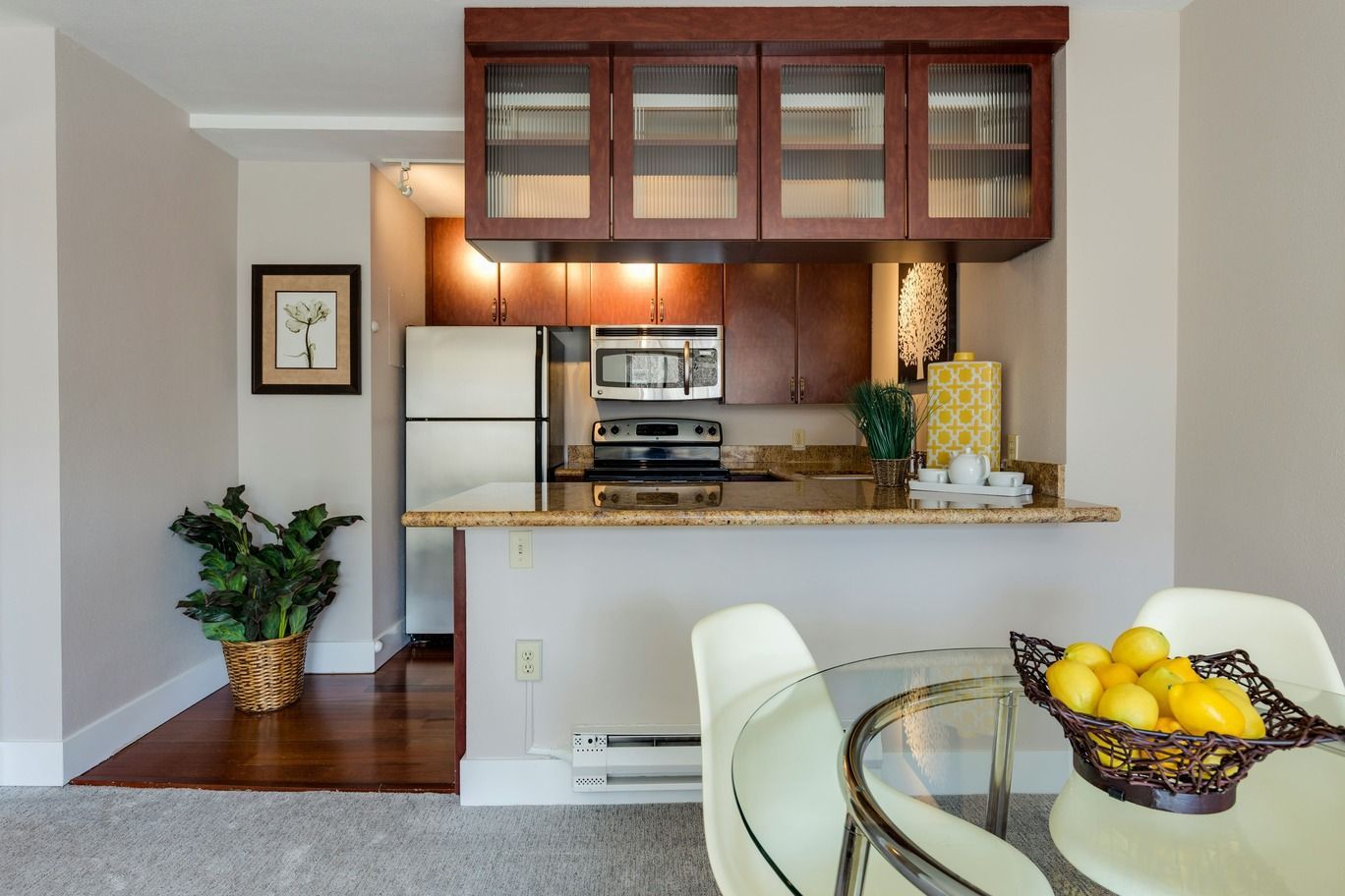 Open kitchen with wood cabinets, granite counter, and glass dining table with a bowl of lemons.