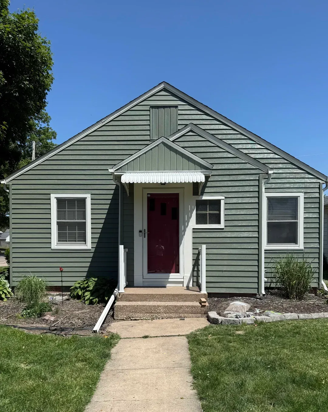 Small gray house with red front door, white trim, and a front walkway under a blue sky