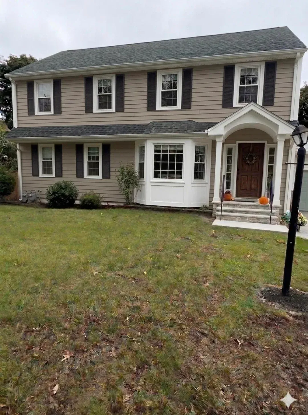Two-story suburban house with gray siding, white trim, and a front lawn on an overcast day