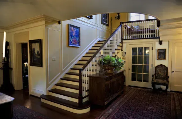 Interior foyer with staircase, glass french doors, framed art, and a wooden console table with plants