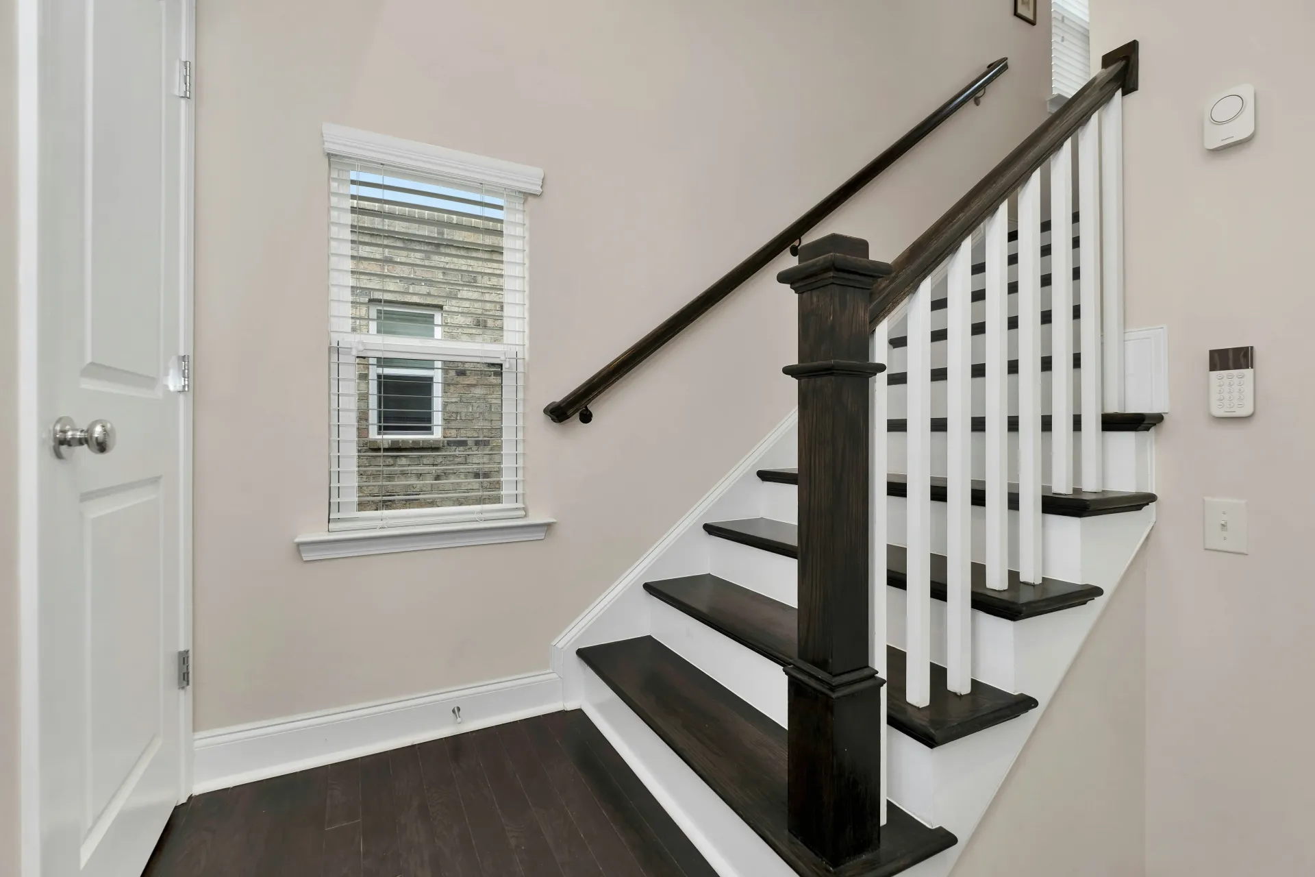 Interior staircase with dark wood railings, white walls, and a small window in a hallway
