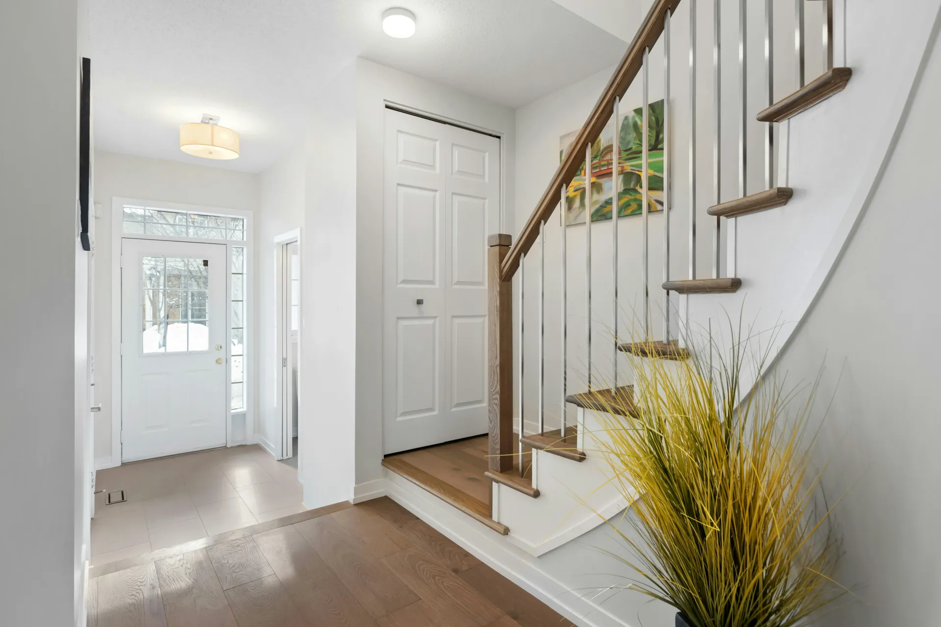 Bright entry hallway with white stairs, wood railing, front door, and a yellow plant arrangement